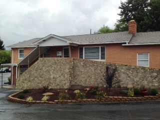 Brick building with a stone retaining wall and landscaped garden in front. The image showcases the property’s exterior and entrance.